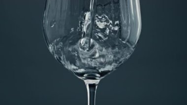 Sparkling water pouring glass at dark background closeup. Air bubbles rising surface. Purified mineral liquid filling splashing in crystal clear cup. Cool refreshing drink in beautiful glassware.