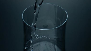 Pure liquid pouring glass top view closeup. Refreshing mineral water splashing in transparent cup. Crystal clear fluid streaming filling simple jug. Cool purified beverage. Health care thirst concept