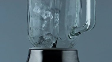 Ice cubes container falling closeup. Cocktail blender filling with iced chunks for summer alcohol beverage. Grinding equipment mixer in kitchen. Evening relaxation party drink preparation concept.