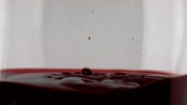 Closeup wine droplets rippling splashing in goblet. Merlot red beverage waving in transparent cup. Commercial shot of bordeaux dripping falling smooth liquor surface. Evening dining enjoyment concept 