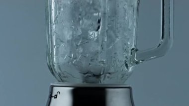 Blender crushing ice pieces closeup. Cocktail mixer grinding cubes for beverage. Barkeeper machine preparing refreshing cool drink for summer party celebration. Mixing iced frozen chunks in container.