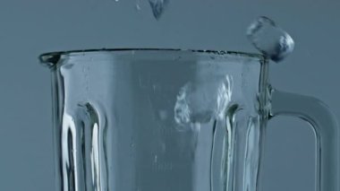 Closeup ice filling blender cup. Making refreshing beverage in cocktail mixer. Diverse cubes falling mixing container. Iced drink preparation on holiday party celebration. Barkeeper equipment concept