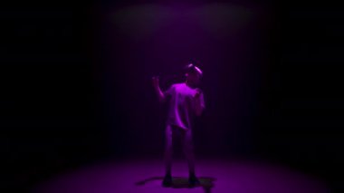 Neon man experiencing virtual reality in dark cyberspace. Focused player explore online simulation in ar headset. Unrecognized gamer enjoying metaverse holding controllers. Teenager lifestyle concept