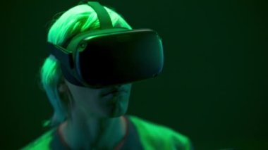 Focused man watching VR headset in neon light closeup. Blonde gamer looking goggles playing videogame over dark multi coloured background. Guy enjoying 3d movie. Future, gadgets, technology concept 