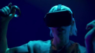 Scared man playing handheld trackpads videogame closeup. Nervous gamer using gadget for virtual reality on neon background. Futuristic goggles youngster testing horror game. Future technology concept 