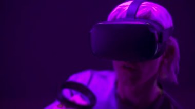 Closeup excited man experiencing VR headset videogame. Impressed gamer using gadget for virtual reality on neon background. Male in futuristic goggles playing controllers. Future technology concept 