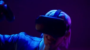 VR headset youngster playing augmented reality simulation. Energetic man expressing interest engaged in futuristic metaverse world using gaming controllers. Future innovation and technology concept
