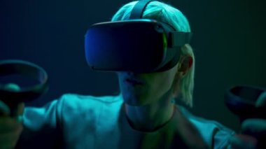 Excited man experiencing handheld trackpads videogame closeup. Impressed gamer using gadget for virtual reality on neon background. Futuristic goggles youngster playing. Future technology concept 