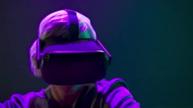 VR glasses person dancing metaverse closeup. Esport blonde gamer using new technology goggles playing game neon light background. Millennial man relaxing with 3d headset. Cyberspace and future concept