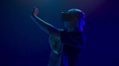 Involved guy visit virtual party closeup. Modern man immersed in abstract neon vr world. Young person augmented reality headset dancing alone slow motion. Metaverse technology future concept