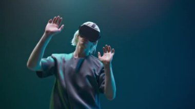 Closeup esport gamer dancing metaverse. VR glasses blonde man using new technology goggles playing game neon light background. Millennial person relaxing with 3d headset. Cyberspace and future concept