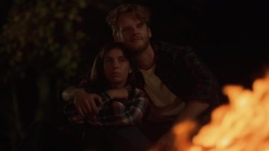 Romantic lovers embrace together on night camping travel journey. Close up young couple enjoy cuddle by burning bonfire outdoors. Loving family hug spend weekend on dark evening date. Love concept.
