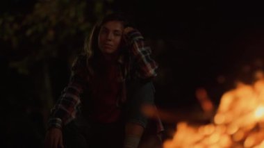 Adventurous girl enjoy campfire burning on dark night outdoors. Close up young millennial woman watch look bonfire on relaxing evening. Tired tourist rest on nature journey. Leisure vacation concept.