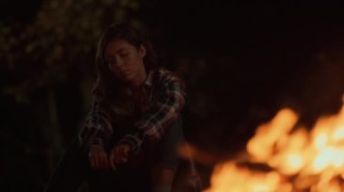 Tired woman look bonfire on dark evening. Close up sad nature explorer sit enjoy camp outside. Troubled tourist think dream freedom on traveling hike. Upset girl watch fire at night. Camping concept.