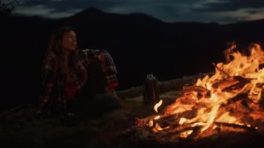 Lonely woman look campfire burn on dark evening. Hipster tourist relax outside on mountains hiking close up. Carefree girl dream freedom wanderlust outdoors. Leisure rest activity lifestyle concept.