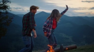 Happy couple dance evening in mountains nature. Tourist family have fun outside close up. Carefree lovers jump by bonfire at sunset evening. Young travelers have fun on active trip. Leisure concept.