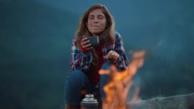 Drinking woman enjoy evening tea by burning camping fire. Close up chill girl enjoy dream in mountains nature. Relaxed tourist spend wanderlust travel on outdoors. Freedom youth recreation concept.