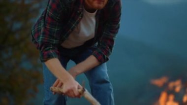Closeup ginger traveler camping on dusk holiday. Young guy enjoy campfire vacation on nature. Smiling tourist spend adventure by fire. Active redhead camper feel freedom wanderlust. Leisure concept.