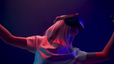 Professional gamer exploring environment in simulation closeup. Young generation z woman in VR helmet using wireless controllers playing at neon light. Modern technologies and metaverse concept