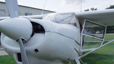 Small private plane parked on green grass aerodrome cloudy day close up. White ultralight airplane standing field ready for flight. Modern aircraft with open door waiting pilot. Aviation concept.
