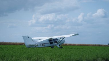 Propeller small airplane parking on green field after long transportation flight. Ultralight white plane with spinning blades turning off engine landing in summer farmland. Private aircraft transport.