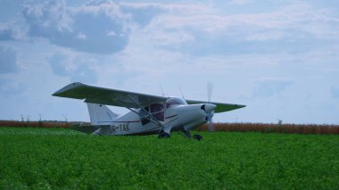 Lightweight airplane standing green field with working propeller preparing to flight. Small private plane with spinning blades parked on grass airfield. View of modern aircraft in front beautiful sky.