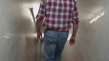 Alt kattaki beyaz koridora bakan adam. Üretim işçisi çiftlik hayvanlarının üretim tesisine gidiyor. Bilinmeyen yönetici müşterisi, sanayi bölgesinde merdivenlerden iniyor..