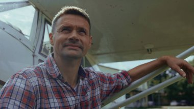 Özel uçak pilotu başarıyla indikten sonra gülümseyerek uçağın yanında oturuyor. Neşeli mühendis işten sonra dinleniyor. Uzağa bakan küçük uçakları koruyor. Havacılık işi havacılık işi konsepti.