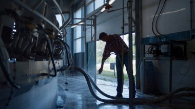 Farmer washing milking system in technological robotic farm using hose. Process of cleaning milk production equipment on modern automated cowshed. Computerized technology dairy producing concept.
