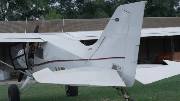 Small ultralight airplane moving back flaps on preflight checking process. White lightweight private plane standing on green grass airfield ready for training flight. Aviation business concept.