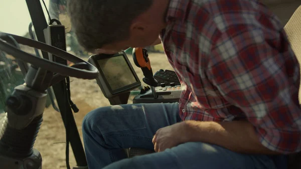 Harvester operator checking machine display closeup. Tractor driver adjusting smart display screen in cockpit. Farming professional driver preparing for autumn wheat harvesting. Automated crop system