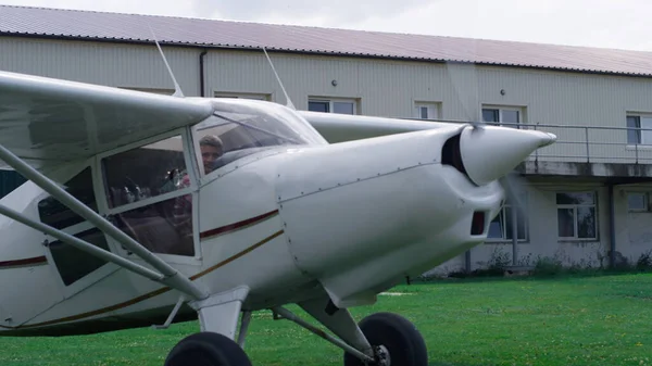 Small airplane starting accelerate ready to fly from green airfield. White lightweight plane with spinning propeller taking off from rural airdrom. Professional pilot sitting in cabin working aircraft