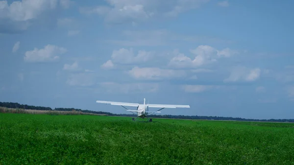 Small private airplane moving on green airfield driving by professional pilot back view. Lightweight white plane with spinning propeller accelerating to take off in blue cloudy sky. Aviation concept.