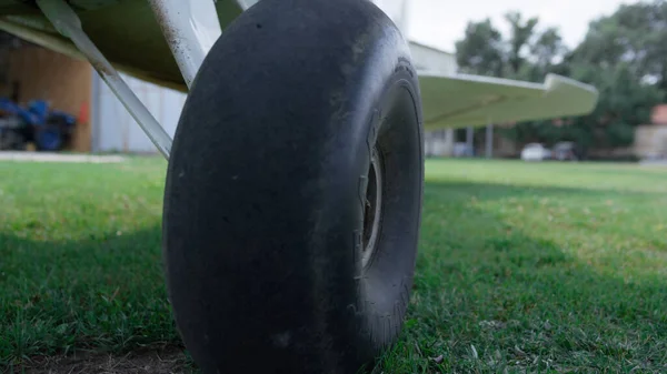 Closeup airplane wheel standing airfield grass. Black plane chassis on green aerodrome field in front hangar. View of part lightweight private aircraft on airdrome. Components of air transport.