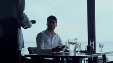 Handsome man customer paying lunch order using smartphone nfc technology in stylish restaurant. Unknown waiter silhouette holding wireless wi-fi credit card reader machine. Contactless payment concept