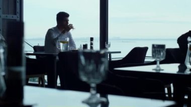 Charismatic man spending lunch time in luxury restaurant. Relaxed businessman drinking refreshing water glass resting in cozy sky bar. Busy ceo manager using smartphone on break in sea cafe.