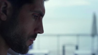 Profile of pensive man resting in stylish restaurant. Bearded hipster guy looking aside in panoramic cafe closeup. Attractive businessman enjoying lunch break. Thoughtful male face expression closeup