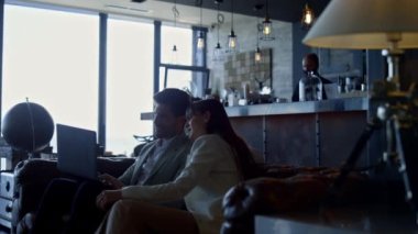 Focused coworkers using laptop in hotel lounge. Entrepreneurs talking solving problem on remote workplace. Business couple discussing marketing project at dark interior place. Busy work concept 