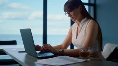 Woman professional surfing laptop at sea panorama window. Office manager working analyzing data online. Focused beautiful freelancer look computer screen reading report. Financial consultant concept.