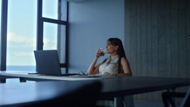 Manager holding whiskey glass resting in office. Pensive woman enjoy alcohol relaxing after work alone. Thoughtful freelancer businesswoman looking window. Depressed executive think business finances