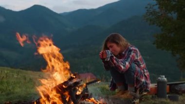 Closeup nature camper relax on nature. Smiling girl enjoy loneliness in mountains. Lonely tourist warm hands by campfire outside. Relaxed hiker spend holiday at hiking trip. Journey leisure concept.