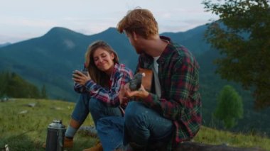 Smiling couple camp mountains on vacation holiday. Two lovers flirt on nature green hill close up. Positive tourists enjoy travel activity together on romantic evening picnic. Happiness love concept.