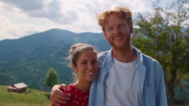 Portrait of cheerful couple looking camera on mountain backdrop. Closeup ginger man hugging smiling woman outdoors in sunny day. Happy pair enjoying summer vacation on nature. Family weekend concept.