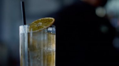 Closeup cocktail lemon glass indoors. Unknown waiter working in restaurant interior. Silhouette bartender making beverages with ice cubes for people in nightclub. Mixology and barman occupation