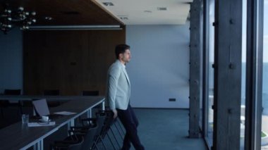 Man enjoying break conference room alone. Businessman ceo thinking life problems dreaming in beautiful sea view luxury office. Peaceful elegant manager making work pause and looking distance 