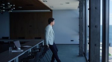 Worker resting luxury office conference room. Company intern taking break looking sea view panoramic window. Businessman manager contemplating project issues. Concerned client waiting lawyer alone 