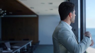 Pensive man ceo watching sea view. Successful businessman thinking analyzing problems and waiting in panoramic window office. Focused serious bearded professional contemplate and adjusts suit alone