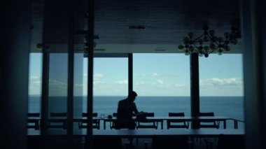 Businessman silhouette reading contract papers at sea view. Unrecognizable thinking manager analyzing data looking panorama window. Unknown focused lawyer checking finance documents corporate report 