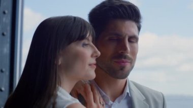 Closeup man kissing woman sea view. Happy couple enjoying romantic date at panoramic window hotel. Portrait of joyful lovers face smiling overlooking ocean. Loving lady putting hands on guy shoulder