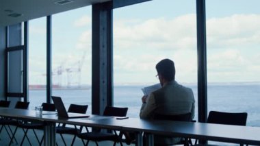 Unknown director reading papers at ocean view. Rich manager checking report at panorama window place rear view. Unrecognized businessman studying deal contract documents at luxury workplace 